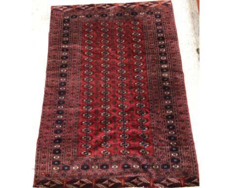 A Bokhara rug, the central panel set with repeating elephant foot medallions on a dark red ground, within a stepped red, blue