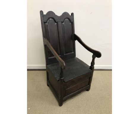 An 18th Century oak lambing chair, the twin fielded arched panel back bearing initials "KE" and date "1738", over a box seat 