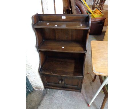 A 61cm vintage Ercol dark elm three shelf waterfall bookcase with shaped sides and double cupboard under