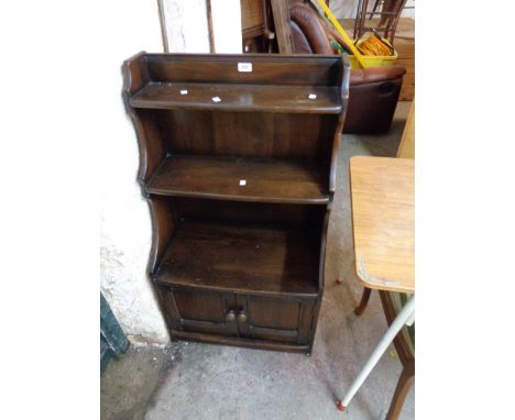 A 61cm vintage Ercol dark elm three shelf waterfall bookcase with shaped sides and double cupboard under