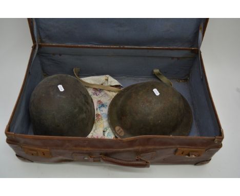 A vintage suitcase containing a WW2 American helmet and a WW2 British helmet.