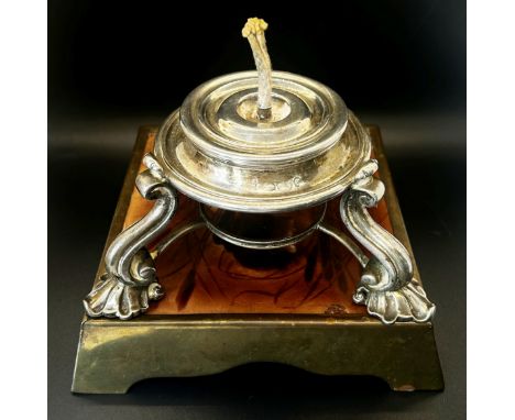 A Victorian silver table lighter with central reservoir on three shell supports, together with a ceramic tile in brass frame 