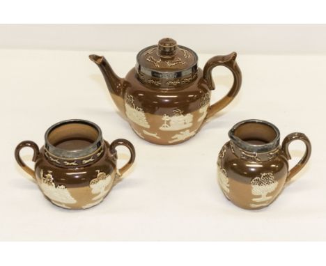 A small salt glazed teapot, sugar and cream with silver collars