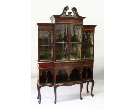 AN EDWARDIAN MAHOGANY BREAKFRONT STANDING BOOKCASE, the top with swan neck pediment, over four glass panel doors, long drawer