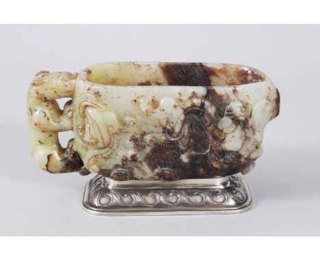 A CHINESE 18TH CENTURY CARVED JADE LIBATION CUP, the sides carved with animals and scrolls, on a silver base. 12cms long.