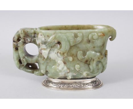 A CHINESE 18TH CENTURY CARVED JADE LIBATION CUP, the sides carved with animals and scrolls, on a silver base. 14cms long.