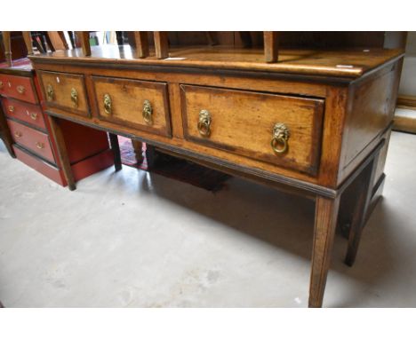 A late Georgian oak dresser base, the oblong top above three crossbanded drawers, each with later moulded brass lion mask and