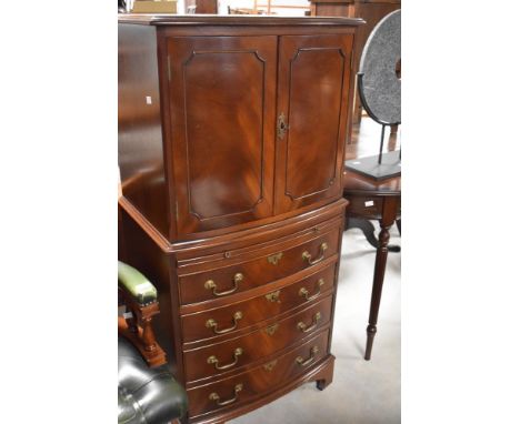 A reproduction mahogany drinks cabinet, the rectangular bow-fronted top over two panelled doors, enclosing the interior with 