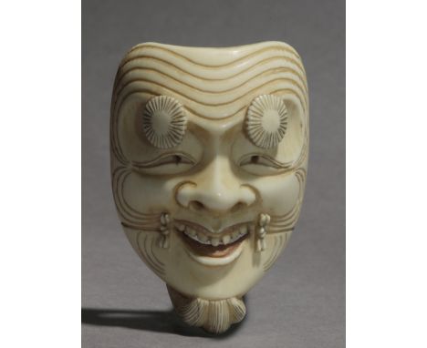 A late 19th century Japanese netsuke from Meiji period. Signed on the back. In carved elephant ivory portraying a mask ogf Ok
