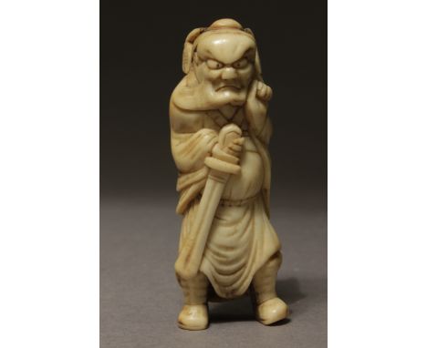A late 18th century Japanese netsuke from Edo period. Not signed. In carved stag horn portraying a standing Shoki gripping a 