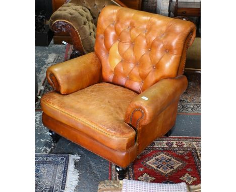 A Victorian style tan leather button backed armchair, raised on turned front legs, uneven colour fading