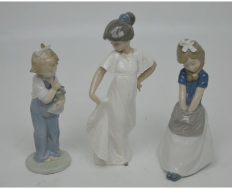 Three Nao figures; a young girl holding her dress, a young girl holding a doll and a girl with an apron (3).