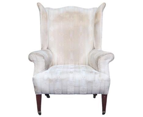 AN EDWARDIAN WINGBACK ARMCHAIR&nbsp; with shaped wingback over scrolled arms on square tapering supports terminating in ceram