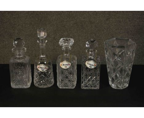 Four cut crystal decanters and a trumpeting form cut crystal vase. Three decanters with ceramic and gilded name labels. H.30 