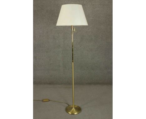 A contemporary brass reading lamp, with an adjustable arm and a pink shade, on a circular base. H.170cm. 
