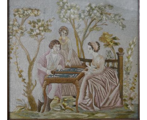 A framed and glazed 19th century silk embroidery of three people playing backgammon in a garden with watercolour detail. H.44