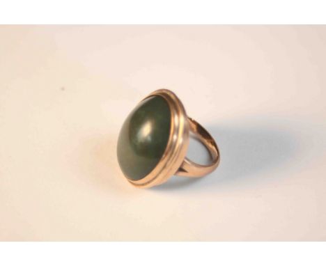 A pink metal (tests as 9ct gold) and green stone cabochon dress ring, set with an oval green hardstone cabochon. Ring size Si