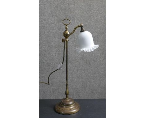 An early 20th century brass student's lamp with handle on a moulded circular base. The bell form shade made of rippled milk g