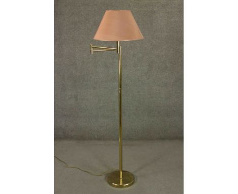 A contemporary brass reading lamp, with an adjustable arm and a pink shade, on a circular base. H.170cm. 