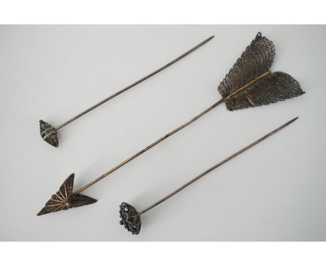 A 1930s white-metal filigree jabot hat pin in the form of an arrow, 21 cm, 17g, tests as silver, together with two further fi
