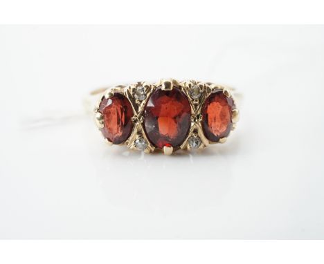 A vintage three-stone garnet and diamond ring, the largest oval cut garnet of approximately 1ct, flanked by two further garne