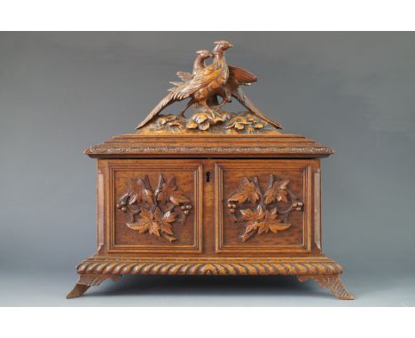 A 19th Century Black Forest type carved walnut two compartment tea caddy, the hinged lid surmounted by a pair of carved pheas