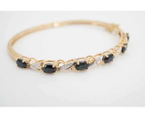 A 9ct gold, sapphire and diamond hinged bangle, with six oval-cut sapphires, each of approximately .60ct, interspersed by dia