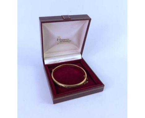 A 9ct gold bangle, with engraved foliate decoration, on a snap clasp, with safety chain as fitted, 10.5g.