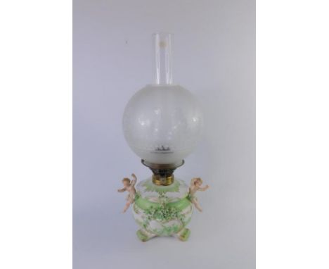 A Continental late 19thC porcelain oil lamp, of circular rococo form with cherub handles, painted in green and encrusted with