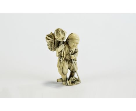 Ivory Figural Netsuke, showing a man walking along with a staff, carrying a creature in a basket on his shoulder; the man wea