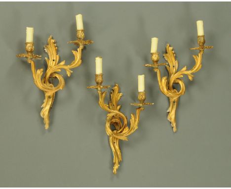 Three gilt metal light fittings, in the rococo style.  Height excluding light fitting 38 cm.