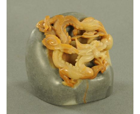 A Chinese small boulder carving, 20th century, with carved dragon chasing a pearl in tones of caramel, all upon a slate grey 