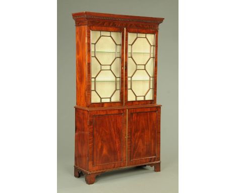 A George III mahogany bookcase on cupboard, having a shaped pediment above the glazed cupboard doors including adjustable she