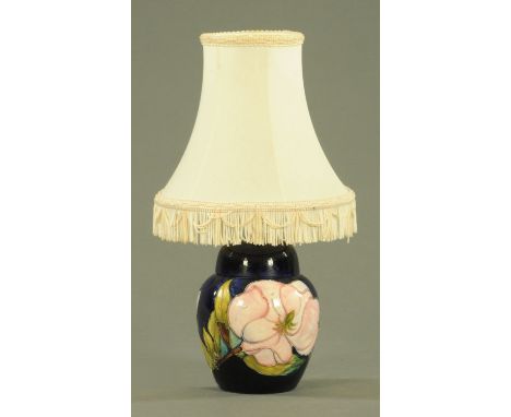 A Moorcroft Magnolia pattern table lamp, 20th century, of ginger jar form against a dark blue ground, green inscribed initial