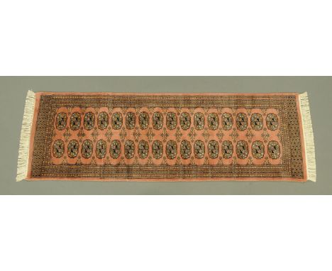 A short runner, with geometric medallions against a light coral ground within a three band border and with knotted fringed en