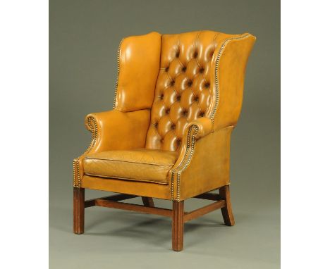 A Georgian style tan leather wing armchair, 20th century, with button back with shaped sides and applied brass stud decoratio