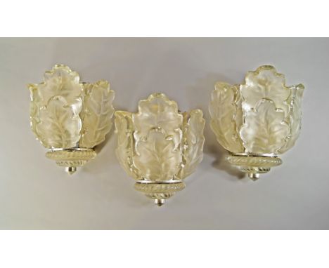 A set of three glass and aluminium framed wall lights, c 1940-1950, the glass shades formed into oak leaves, above tiered bas