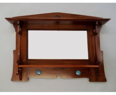 An Arts & Crafts walnut two tier wall shelf and mirror, the shelves with pierced stylized tulip supports, flanking a beveled 