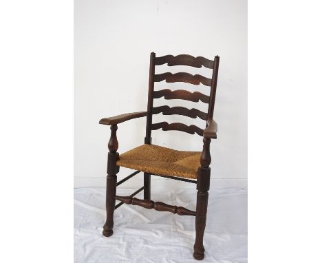 EDWARDIAN OAK FRAMED ELBOW CHAIRwith shaped ladder back, rush covered seat, raised on turned front legs and stretcher