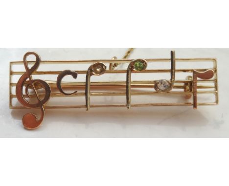 UNUSUAL GEM SET NINE CARAT GOLD BROOCHin the form of a musical scale with a treble clef and three notes, one set with peridot