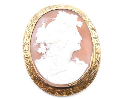 A yellow metal framed carved cameo brooch pin. The brooch pin having an oval carved cameo depicting the profile of a lady fac