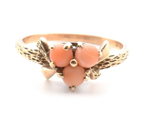 A hallmarked 9ct gold and coral ring. The ring set with three round cabochons of coral set in an abstract textured mount to t