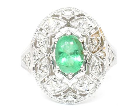 A 18ct white gold emerald and diamond cluster ring. The ring set with an oval cut emerald to a pierced diamond millegrain dec