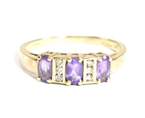 A hallmarked 9ct gold, amethyst and diamond ring. The ring having three oval cut amethysts flanked by two columns of three ch