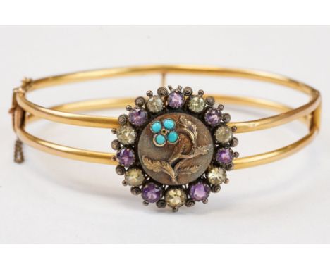 Late Victorian / Edwardian amethyst, citrine and turquoise yellow metal hinged bangle; the central metal panel with cast flow