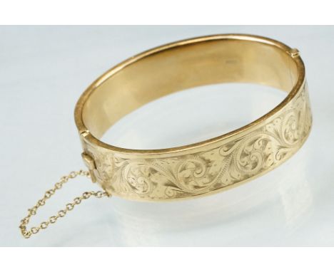 9ct yellow gold hinged bangle, engraved foliate scroll decoration to the upper half, tongue and box clasp, safety chain, widt