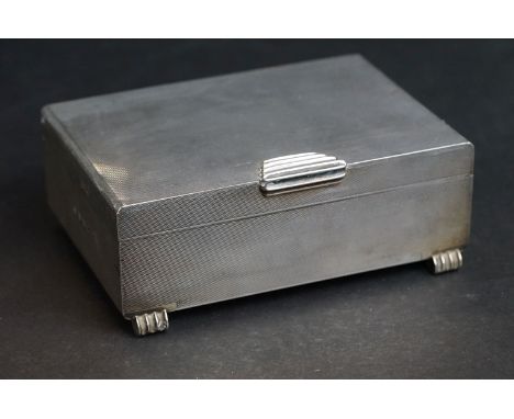 Silver cigarette case, tapered ribbed thumbpiece to the hinged lid, engine turned decoration, the body raised on four feet, m