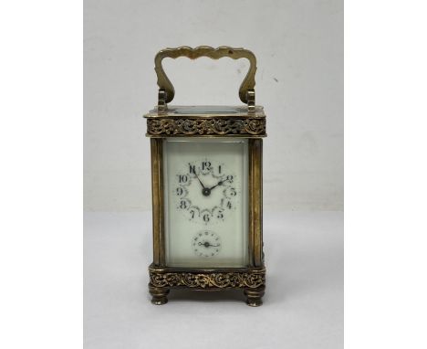 A French small brass Carriage Clock with hinged handle, floral scrolled frieze decoration, the white enamel dial decorated ga