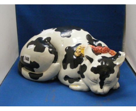 A good sized antique ceramic figure of a black and white sleeping cat wearing a brightly coloured collar. Length 33cms.