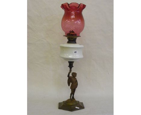 An antique oil lamp with cranberry glass shade above a white glass reservoir over a figural stem in the form of a gentleman d